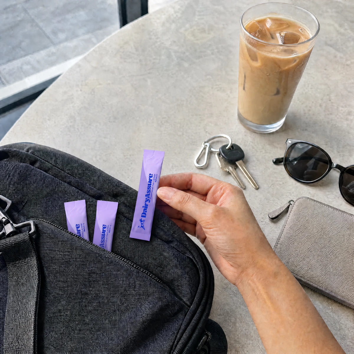DairyAssure lactase sticks packed beside an iced coffee for on-the-go use